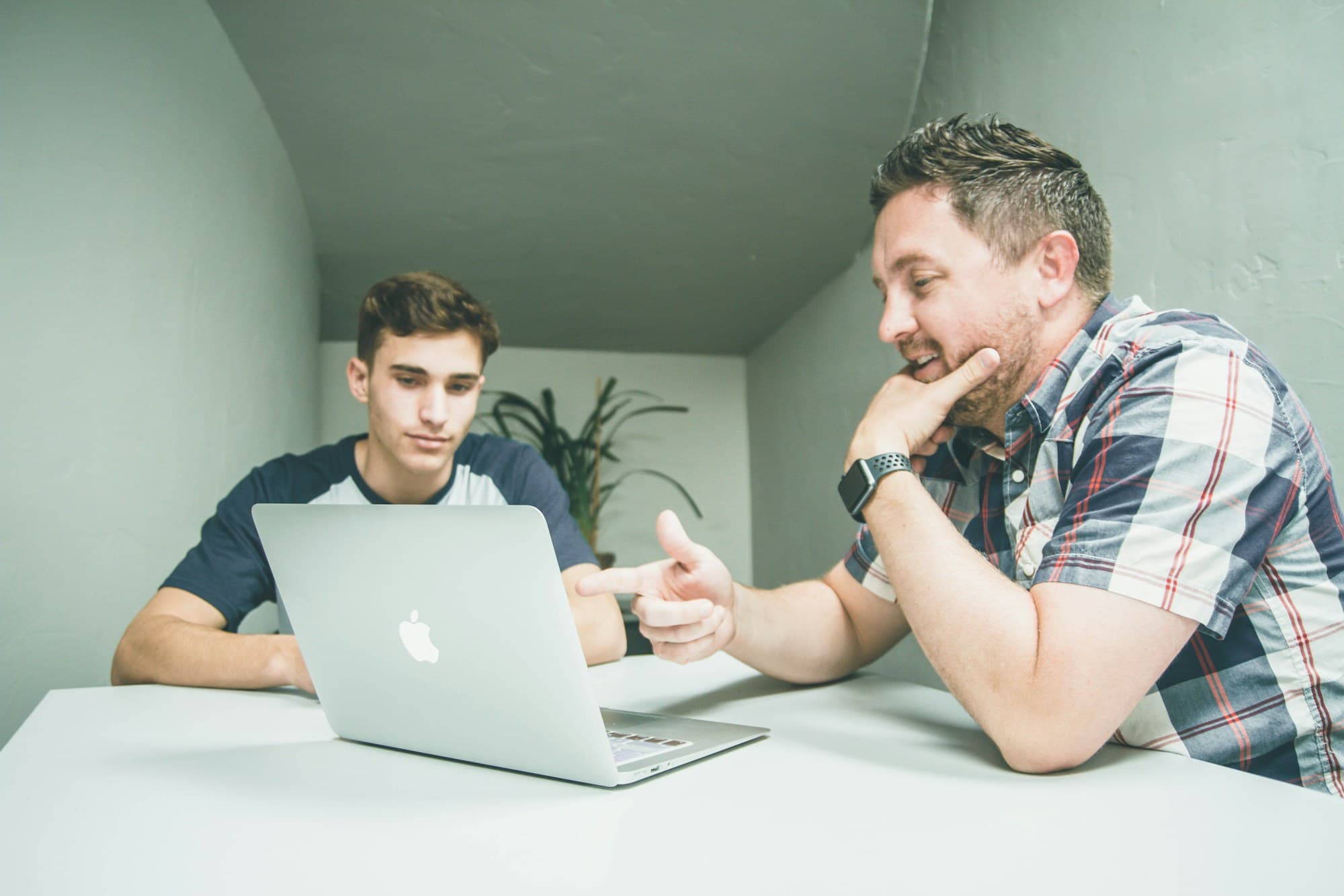 A manager rests his chin on his hand while pointing something out on a colleague's laptop screen, both concentrating.