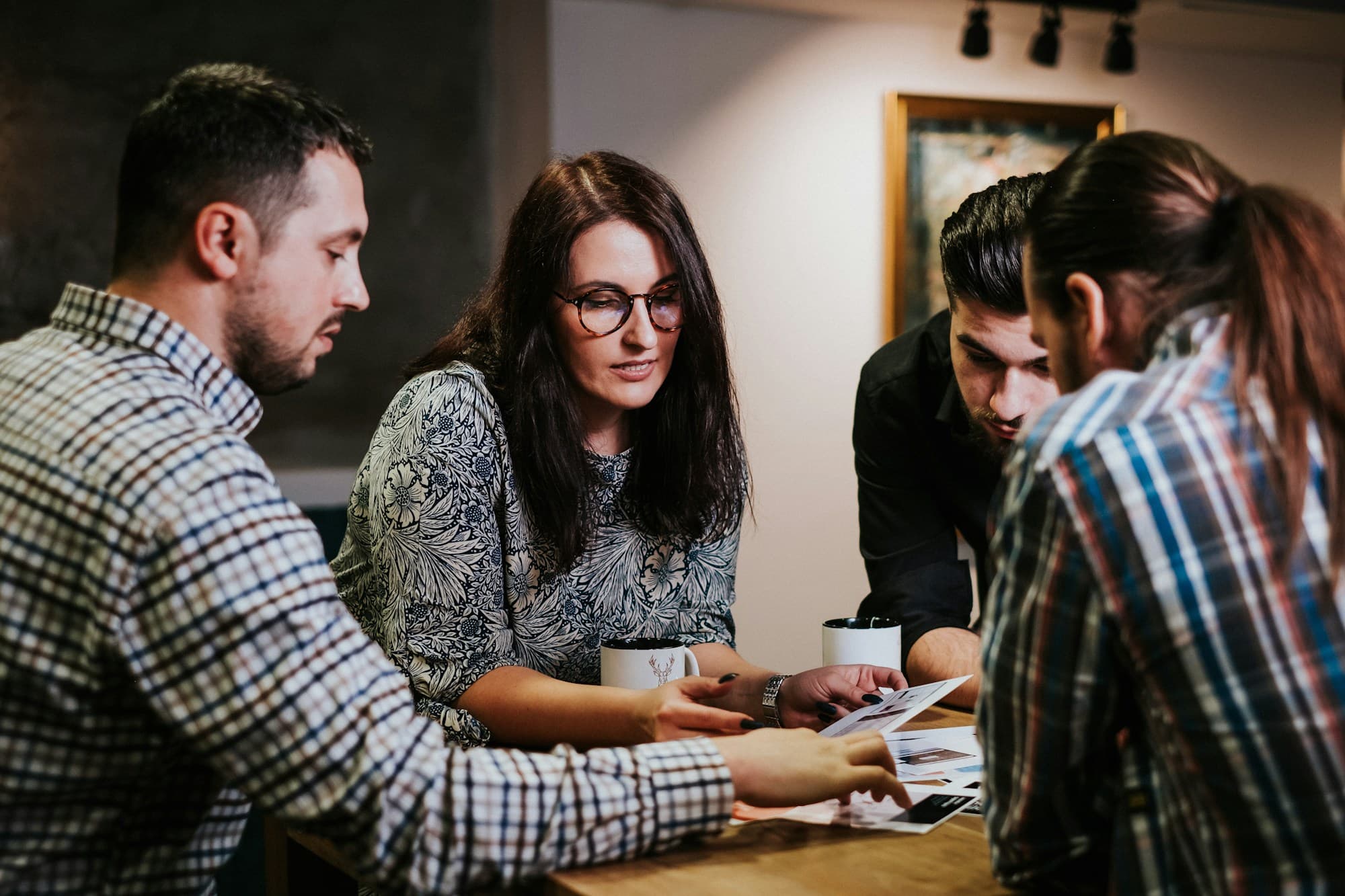 Five colleagues lean in around a wooden table, sorting through printed photos and papers together.