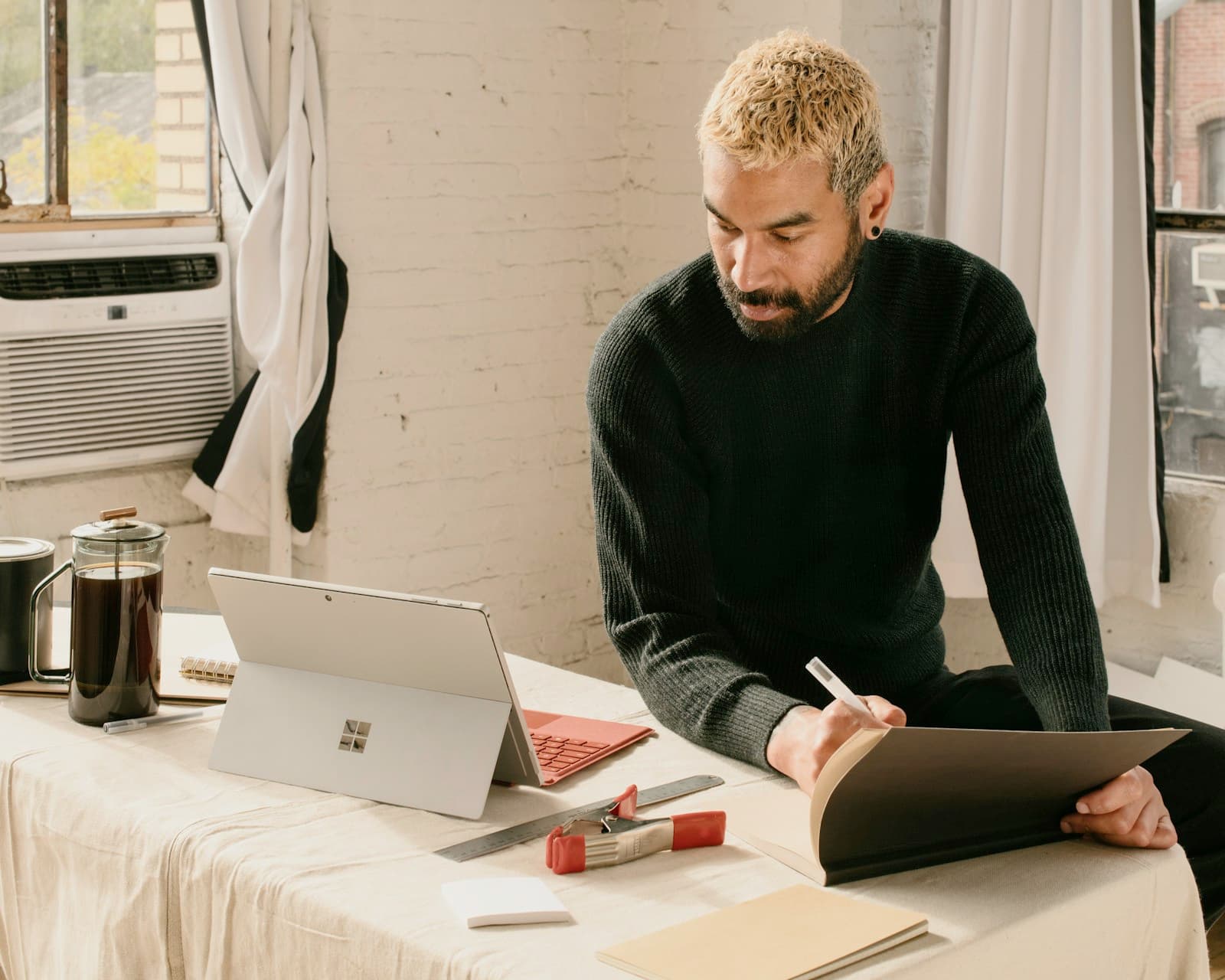Someone leaning over a table at home, reviewing a folder of notes beside their laptop and a cup of coffee.